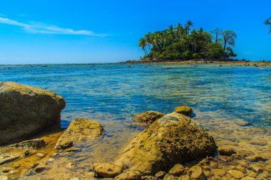 Rock plaj ve deniz suyu mavi gökyüzü ve bulutlu gün arka plan gerilemiştir zaman ağaç ile yalnız uzak ada