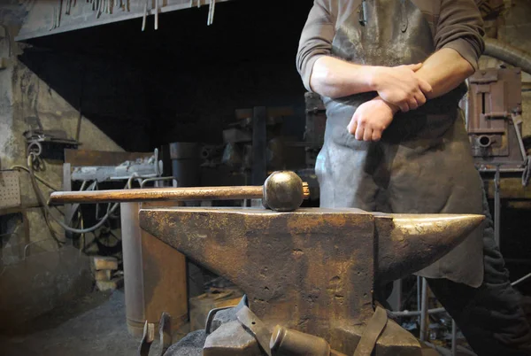 Corps de forgeron avec les mains croisées derrière l'enclume avec un marteau dessus dans la forge — Photo