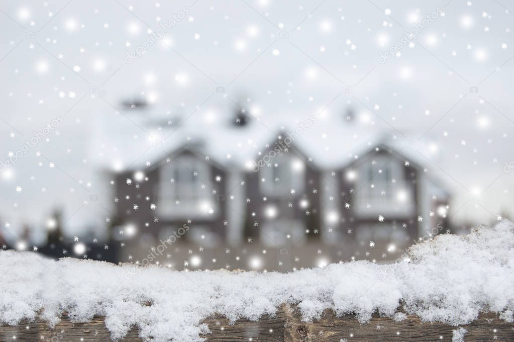 Defocused country house with car and fence in snow. Wooden plank in snow in front side.