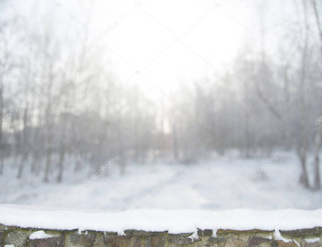 Blurred winter forest background in snow. Old stone fence on the foreground