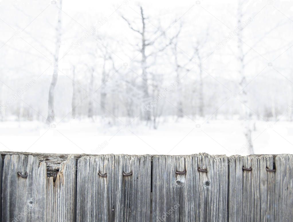 Blurred winter forest background in snow. Old wooden fence on the foreground