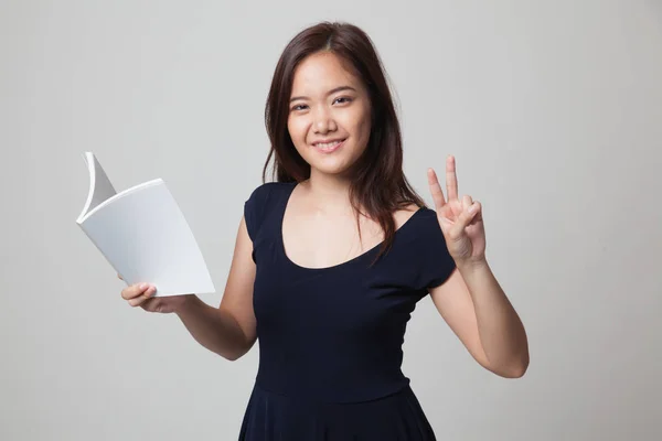 Jonge Aziatische vrouw Toon victor teken met een boek. — Stockfoto