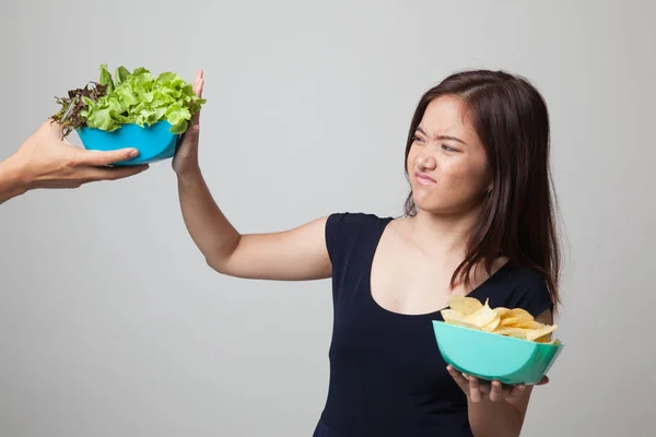 Jonge Aziatische vrouw met aardappel chips nee zeggen tegen salade. — Stockfoto