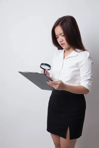 Ung asiatisk kvinna med ett förstoringsglas kontrollrapporten. — Stockfoto