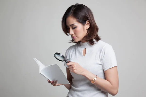 Aziatische vrouw met een boek en vergrootglas. — Stockfoto