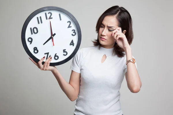 Schläfrige junge asiatische Frau mit einer Uhr am Morgen. — Stockfoto