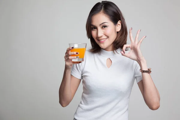 Jovem mulher asiática beber suco de laranja mostrar sinal OK . — Fotografia de Stock