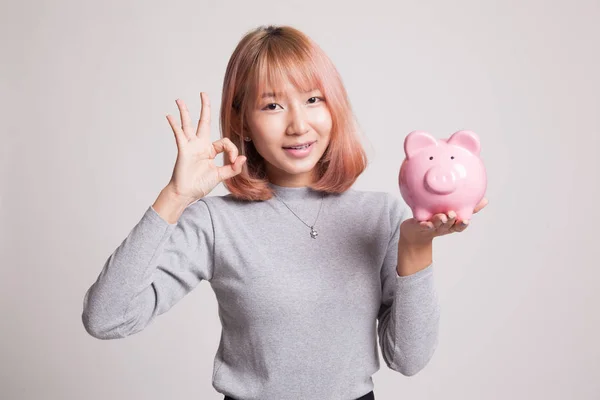 Asian woman show OK  with pig coin bank. — Stock Photo, Image