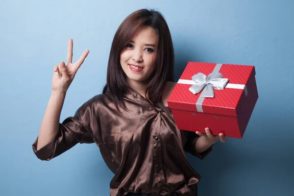 Jovem mulher asiática mostrar sinal de vitória com uma caixa de presente . — Fotografia de Stock