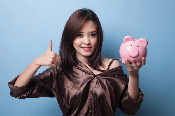 Asian woman thumbs up with pig coin bank.