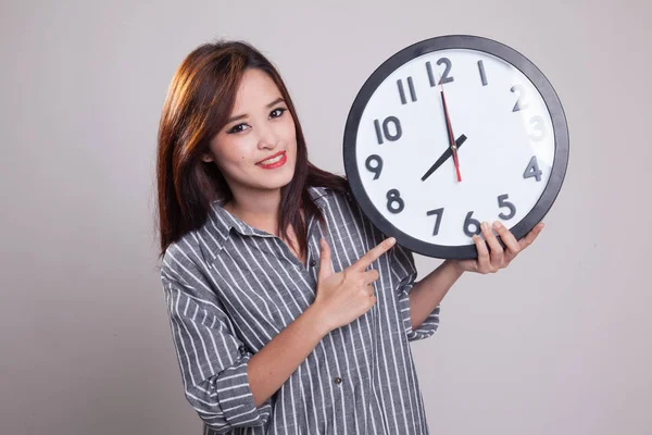 Junge asiatische Frau zeigt auf eine Uhr. — Stockfoto