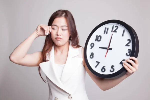 Schläfrige junge asiatische Frau mit einer Uhr am Morgen. — Stockfoto