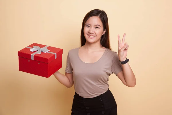 Giovane donna asiatica mostra segno di vittoria con una scatola regalo . — Foto Stock