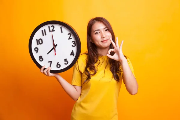 Young Asian woman show OK with a clock in yellow dress — Stock Photo, Image