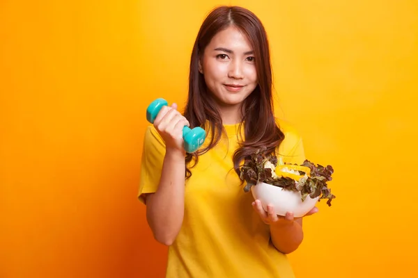Здоровая азиатка с гантелями и салатом в желтом платье — стоковое фото