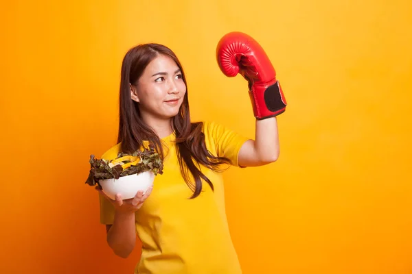 Jonge Aziatische vrouw met bokshandschoen en salade in gele jurk — Stockfoto