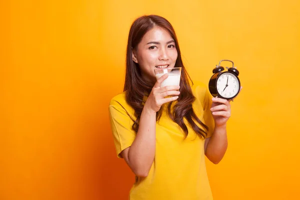 健康亚洲妇女喝玻璃牛奶保持时钟在黄色 — 图库照片