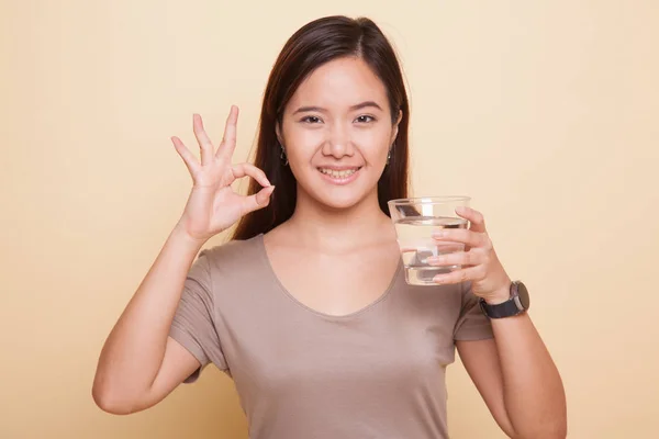 Junge asiatische Frau zeigen ok mit einem Glas Trinkwasser. — Stockfoto