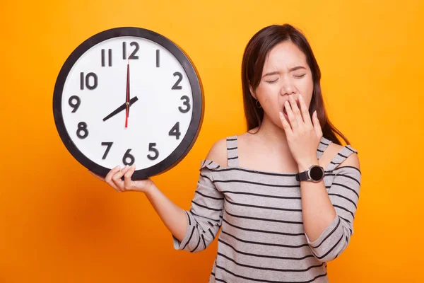 Schläfrige junge asiatische Frau mit einer Uhr am Morgen. — Stockfoto