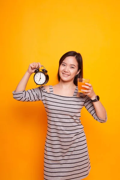 Asian woman with a clock drink orange juice.