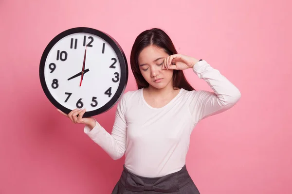 Schläfrige junge asiatische Frau mit einer Uhr am Morgen. — Stockfoto