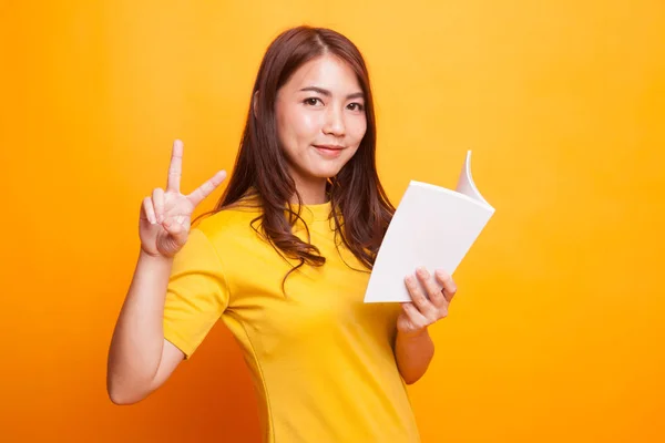 Junge asiatische Frau zeigt Siegerzeichen mit einem Buch. — Stockfoto
