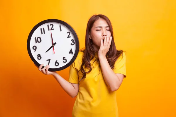 Sleepy joven mujer asiática con un reloj en la mañana en d amarillo — Foto de Stock