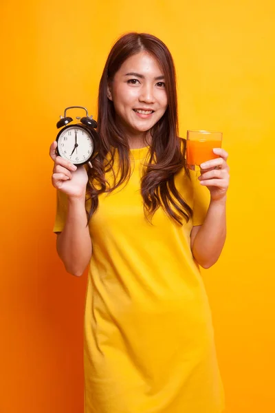 有时钟的亚洲妇女在黄色礼服喝橙汁 — 图库照片