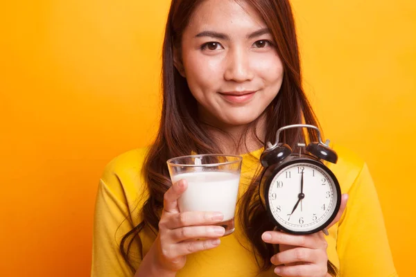 Gesunde asiatische Frau trinkt Glas Milch halten Uhr in gelb — Stockfoto