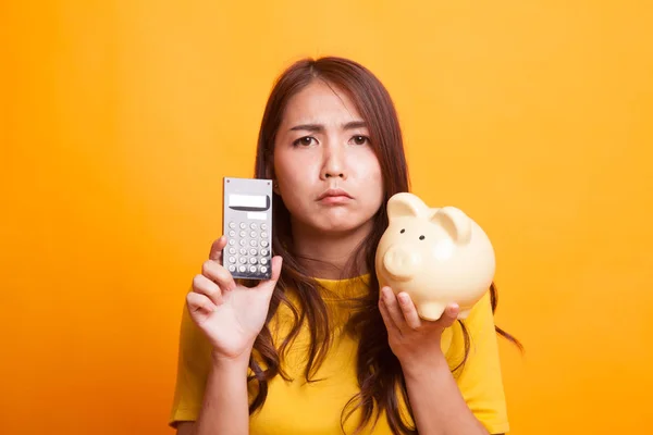 Unglückliche asiatische Frau mit Taschenrechner und Sparschwein in gelb dre — Stockfoto