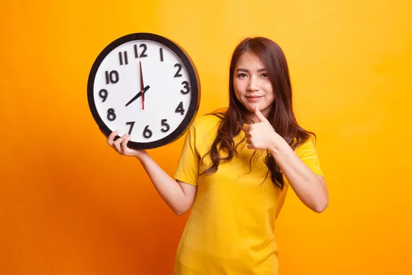 Young Asian woman thumbs up with a clock in yellow dress — Stock Photo, Image