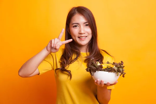 Здоровая азиатка показывает знак победы с салатом в желтом платье — стоковое фото