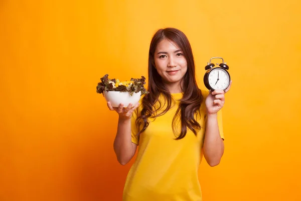 Jeune femme asiatique avec horloge et salade en robe jaune — Photo