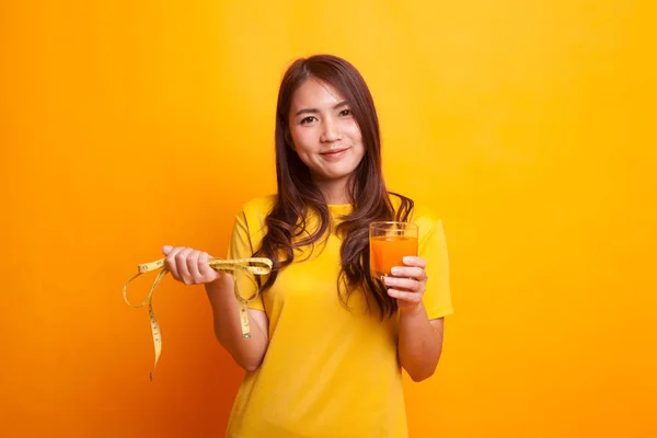 Азиатская женщина пьет апельсиновый сок держать измерительную ленту в желтой дре — стоковое фото