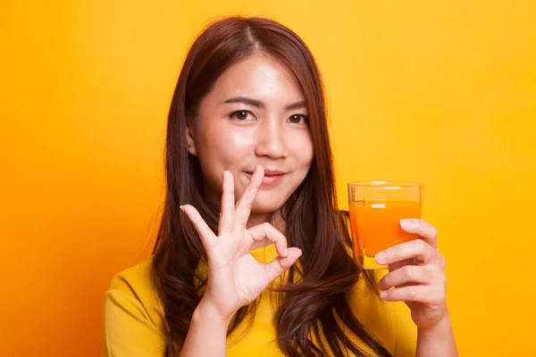 若いアジア女性ショー [ok] は、黄色のドレスでオレンジ ジュースを飲む — ストック写真