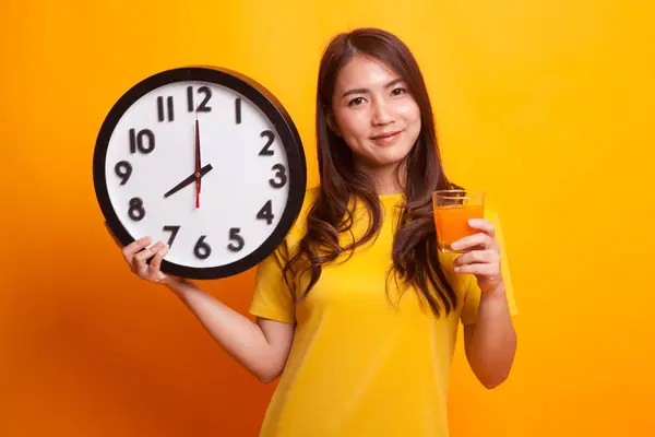 Femme asiatique avec une horloge boire du jus d'orange en robe jaune — Photo