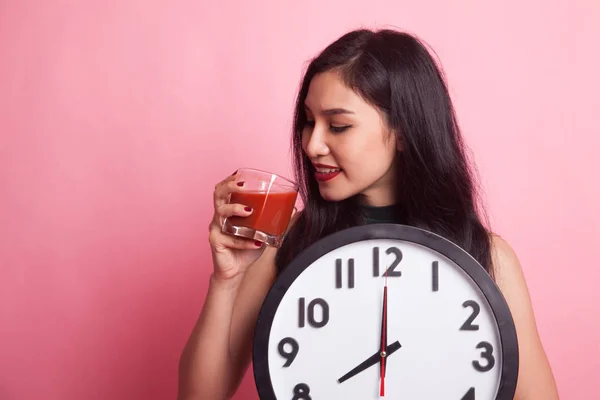 Mladá asijská žena s rajčatovou šťávu a hodiny. — Stock fotografie