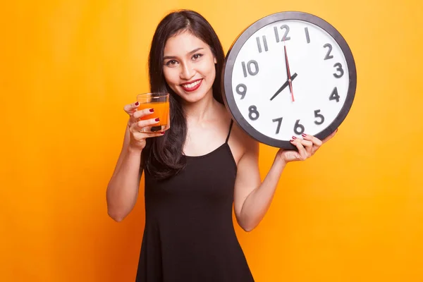 Asian woman with a clock drink orange juice.