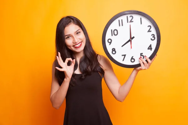 Sleepy young Asian woman with a clock in the morning.