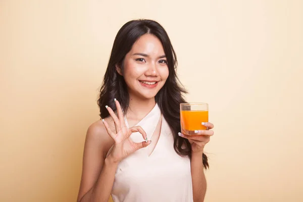 Young Asian woman drink orange juice show OK sign. — Stock Photo, Image