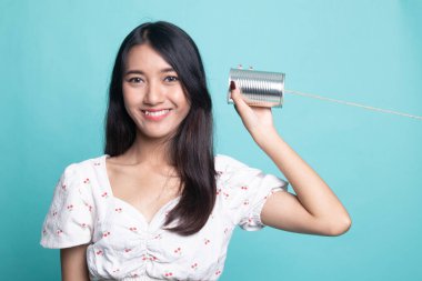  Cyan arka planında teneke kutu telefonu olan genç Asyalı kadın.