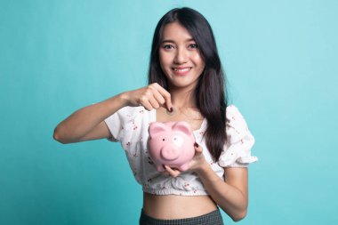 Cyan arka planında para ve domuz sikkesi olan Asyalı kadın.