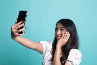Cyan arka planında cep telefonu olan genç Asyalı kadın selfie 'si.