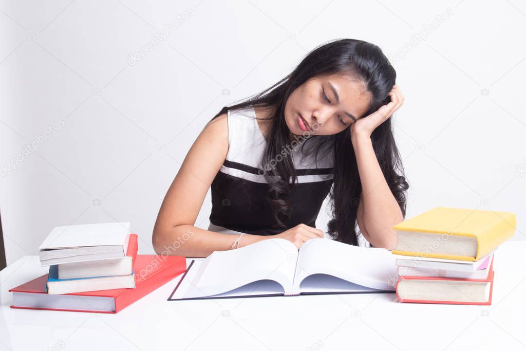 Exhausted Young Asian woman read a book with books on table.