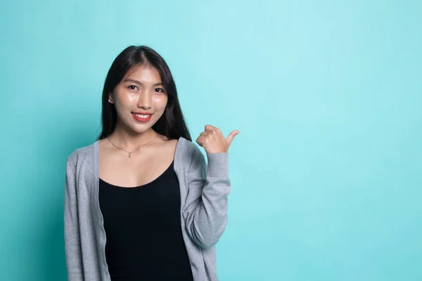 Jovem mulher asiática sorrir e apontar para copiar espaço com o polegar . — Fotografia de Stock