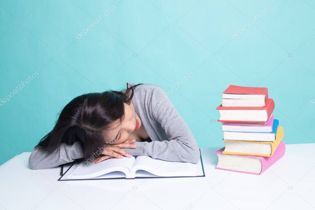 Exhausted Young Asian woman sleep with books on table.