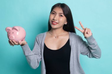 Asyalı kadın göstermek zafer işareti domuz para banka ile.