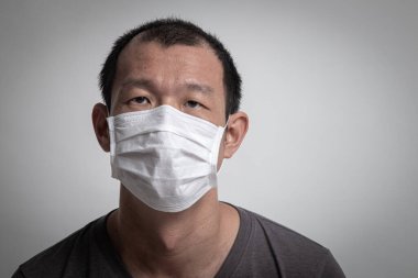 Grip virüsünü önlemek için cerrahi maske takan Asyalı adam ve beyaz arka planda Pm2.5 toz bulutu hava kirliliği