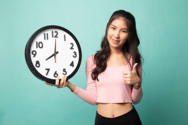 Genç Asyalı kadın, Cyan arka planında bir saat ile baş parmağını kaldırdı