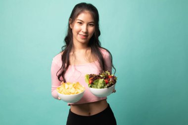 Cyan arka planında patates cipsi ve salata olan genç Asyalı kadın.